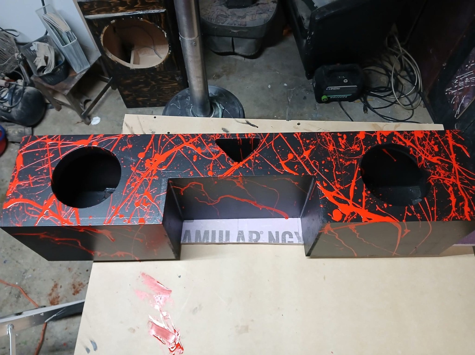 Long black enclosure with red splatter, two subwoofer openings and a center recess
