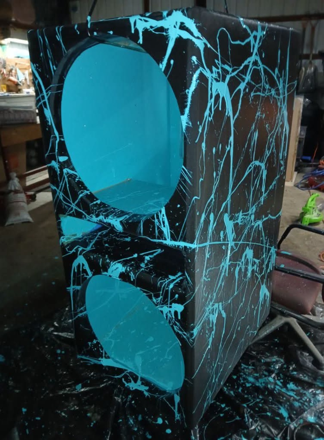 Black dual-subwoofer enclosure with turquoise splatter and matching interior