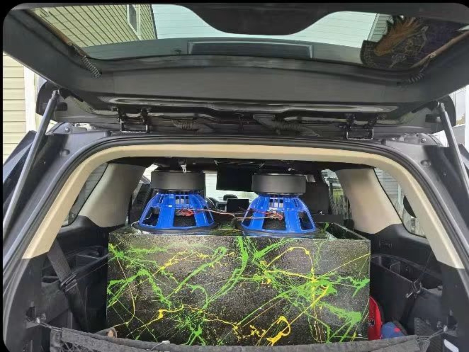 Green and yellow splatter enclosure with two inverted blue subwoofers installed in a vehicle