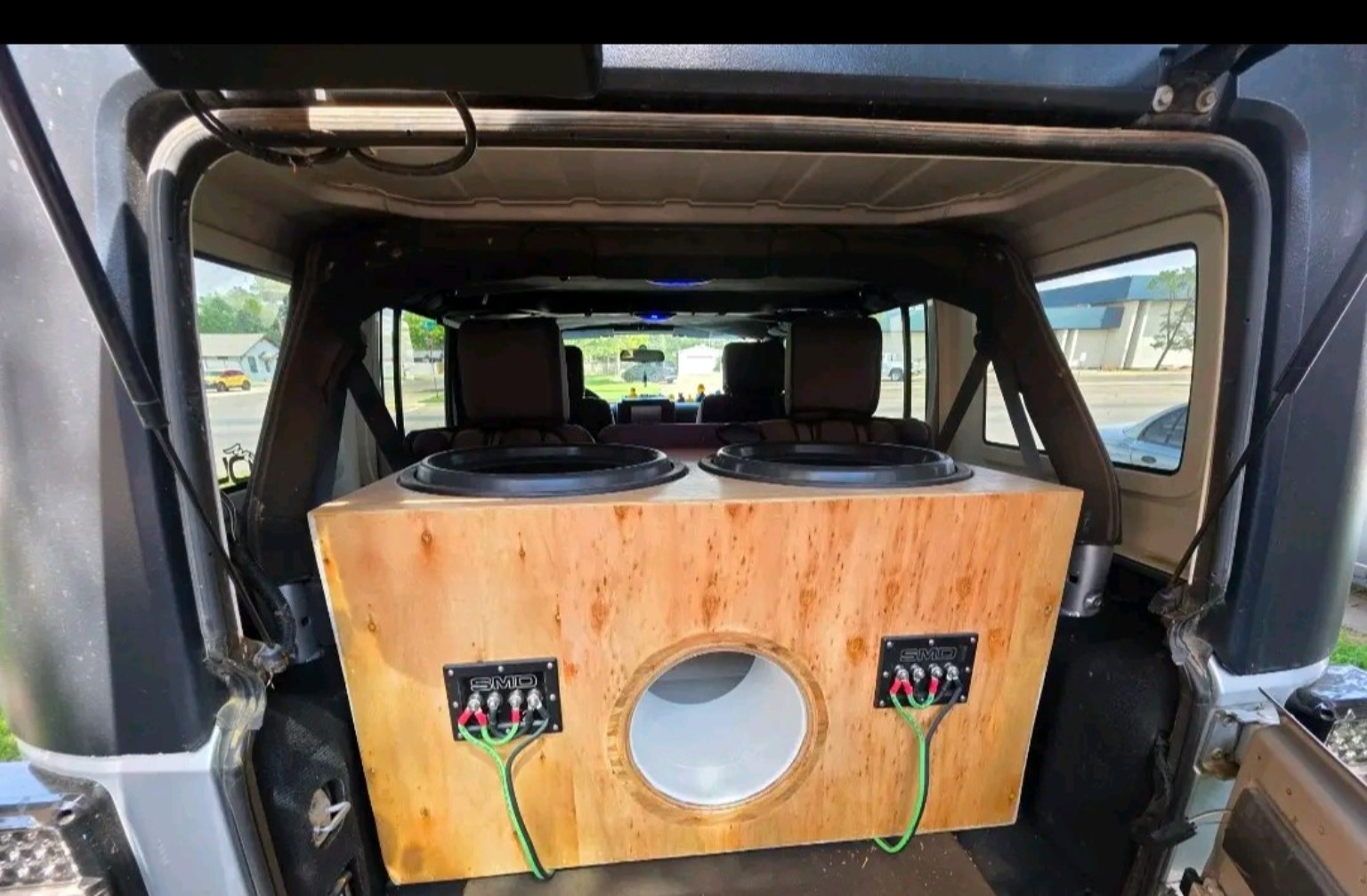 Natural wood dual-subwoofer enclosure with a round port installed in a vehicle
