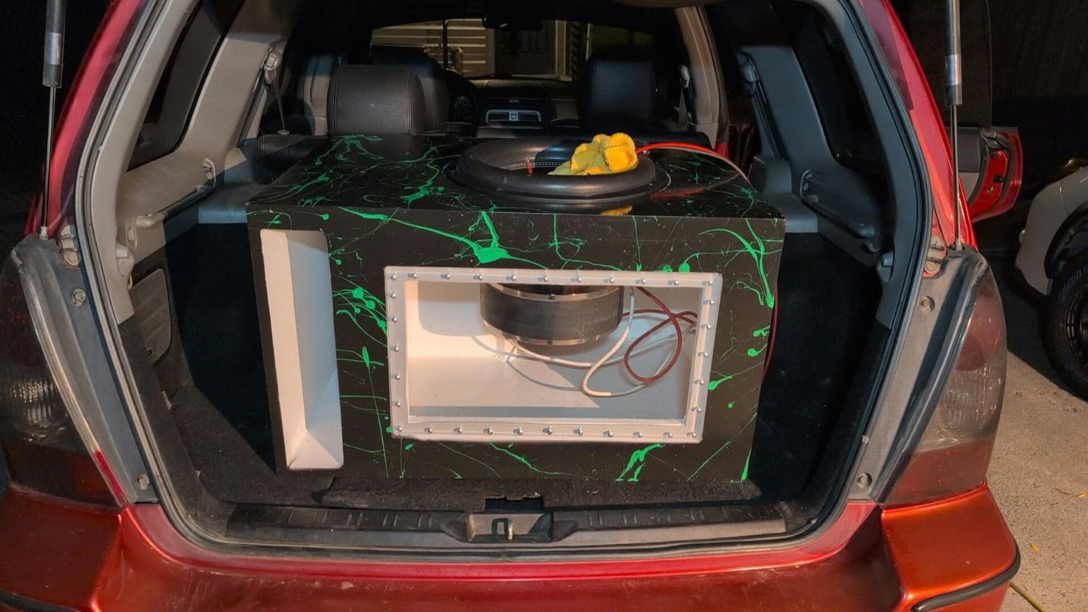 Black and green splatter subwoofer enclosure with a clear window installed in a red SUV
